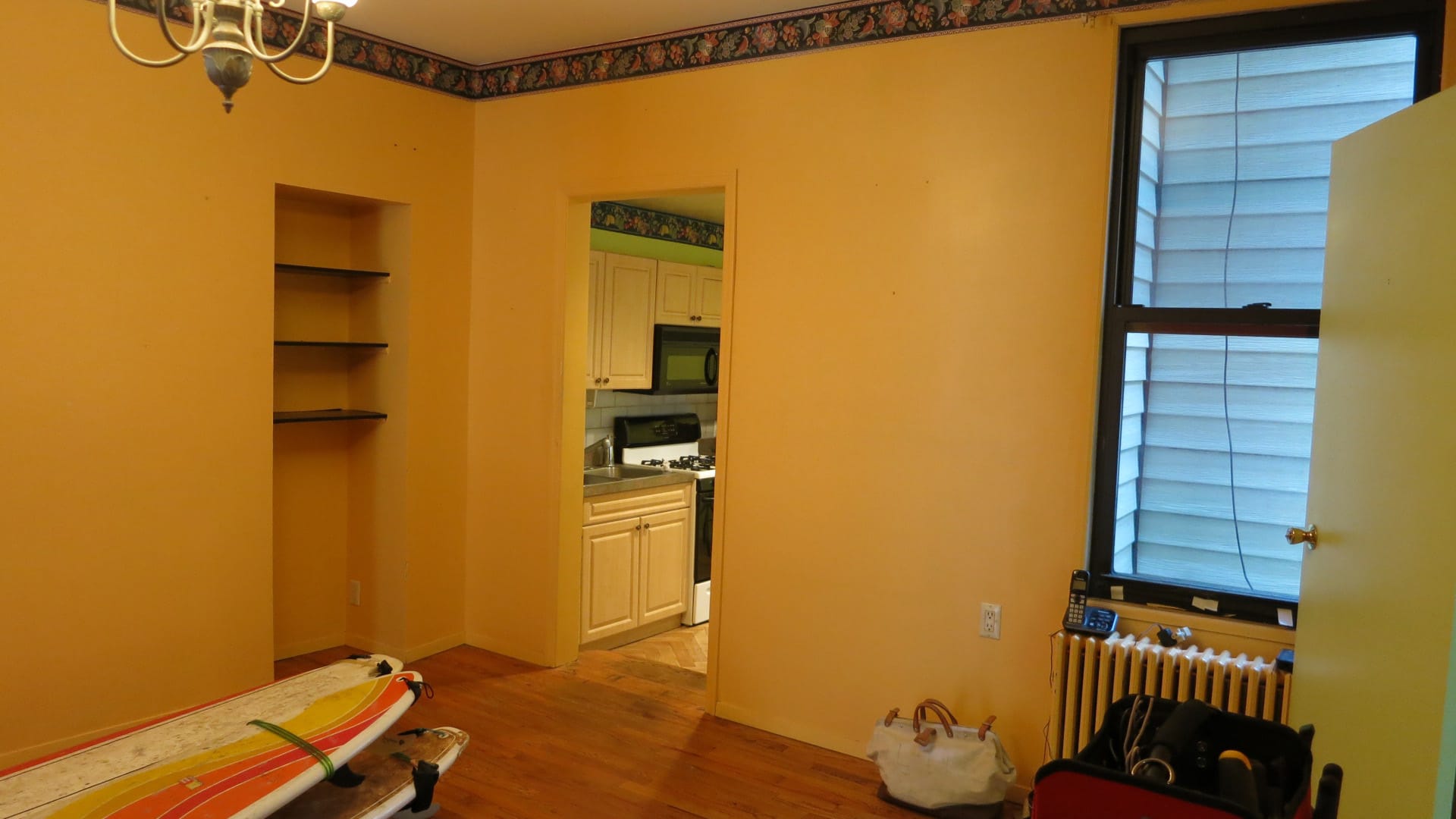 Kitchen before renovation with tan walls, wood floors, and two surfboards at the bottom left.